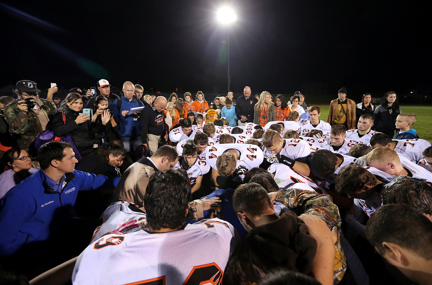 In this Friday, Oct. 16, 2015, photo, Bremerton assistant football coach Joe Kennedy, obscured at center in blue,  is surrounded by Centralia players after they took a knee with him and prayed after their game against Bremerton, in Bremerton, Wash. The Washington coach who was told by district officials to stop leading prayers after games went ahead with a prayer at the 50-yard line after a weekend game. (Meegan M. Reid/Kitsap Sun via AP)